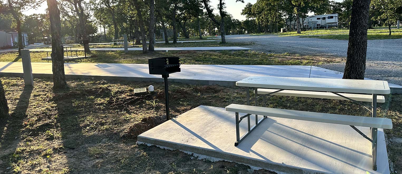 A cement slab site at Hog Mountain RV Ranch with a picnic table and a pedestal grill under oak trees